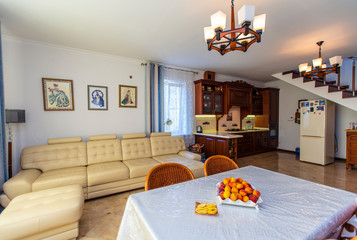 Classic bright living room with wooden furniture in the house. In the center is a table with fruit and four wicker chairs. White large leather sofa.  Antique Sideboard made of wood. 