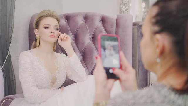 The girl is photographed on the phone. Photo session on the phone. Beautiful girl takes a selfie. The bride takes a selfie on her phone. A beautiful woman is sitting on a purple chair.