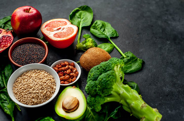 Selection of healthy food:  fruits, seeds, cereals, superfoods, vegetables, leafy vegetables on a stone background. Healthy food for humans. Copy space for your text.