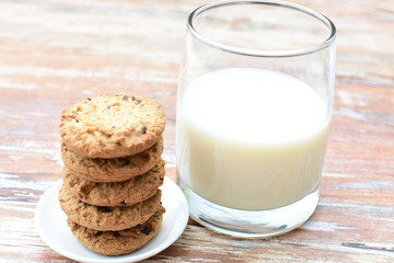 Oatmeal cookies and chocolate chips accompanied by glass of milk