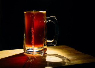 Beer mug with dark beer on a black background, illuminated by a lamp. Beer flows through the glass. Bubbles in a liquid. Concept - natural product, pub, splash screen.