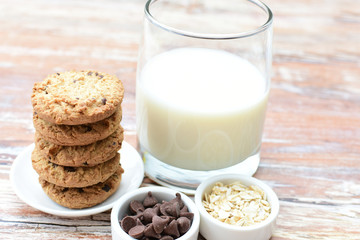 Oatmeal cookies and chocolate chips accompanied by glass of milk