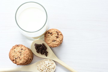 Oatmeal cookies and chocolate chips accompanied by glass of milk