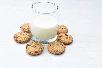 Oatmeal cookies and chocolate chips accompanied by glass of milk