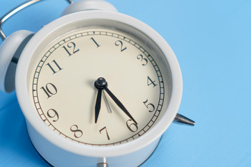 Classic analog gray alarm clock with black arrows on a blue wooden background