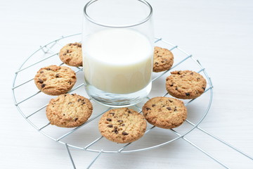 Oatmeal cookies and chocolate chips accompanied by glass of milk