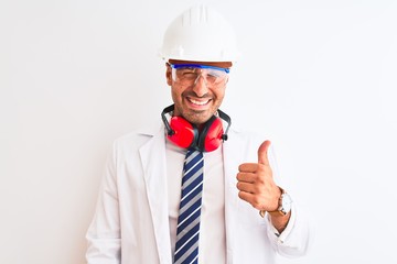 Young chemist man wearing security helmet and headphones over isolated background doing happy thumbs up gesture with hand. Approving expression looking at the camera with showing success.