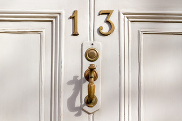 House number 13 on a white wooden front door with bronze door handle