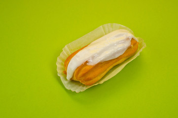 Eclair cake with custard lying on a paper substrate, photographed against a green background. Background for cooking and sweets.