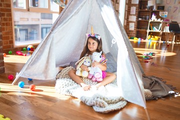 Adorable toddler sitting on the floor inside tipi around lots of toys at kindergarten © Krakenimages.com