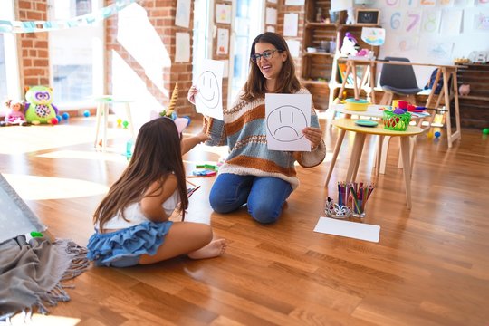 Beautiful pshychologist and toddler doing therapy with emotions emoji around lots of toys at kindergarten