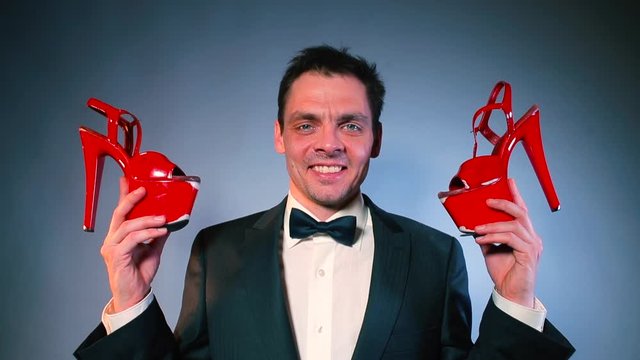The dominant man holds female red shoes in his hands. A man examines the shoes, nuzzles them. Concept of deviant behavior, shoe fetish.