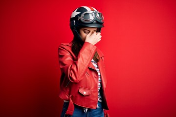 Young beautiful brunette motocyclist woman wearing motorcycle helmet and red jacket tired rubbing nose and eyes feeling fatigue and headache. Stress and frustration concept.
