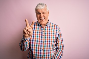 Senior handsome hoary man wearing casual colorful shirt over isolated pink background smiling with happy face winking at the camera doing victory sign with fingers. Number two.