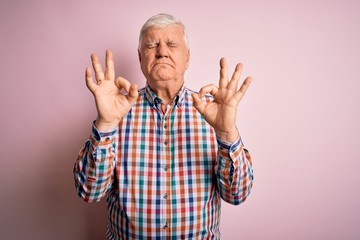 Senior handsome hoary man wearing casual colorful shirt over isolated pink background relaxed and smiling with eyes closed doing meditation gesture with fingers. Yoga concept.
