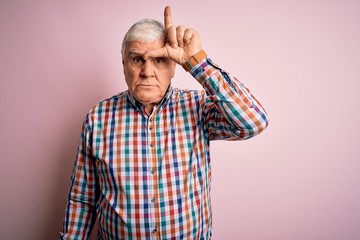 Senior handsome hoary man wearing casual colorful shirt over isolated pink background making fun of...