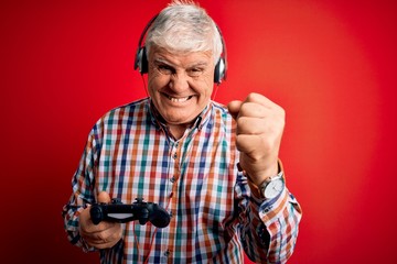 Senior handsome hoary gamer man playing video game using joystick and headphones annoyed and frustrated shouting with anger, crazy and yelling with raised hand, anger concept © Krakenimages.com