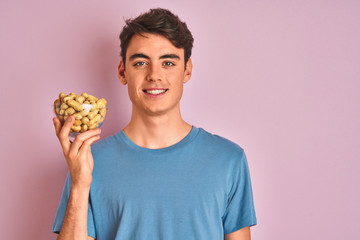 Teenager boy holding a bunch of peanunts over isolated pink background with a happy face standing and smiling with a confident smile showing teeth