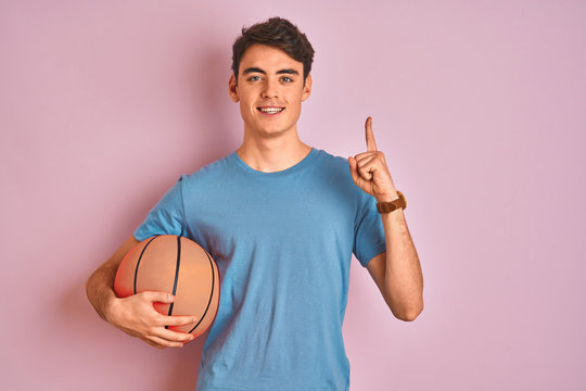 Teenager boy holding professional basket ball over isolated pink background surprised with an idea or question pointing finger with happy face, number one