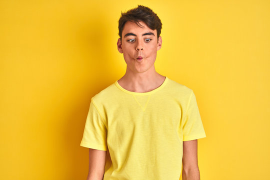 Teenager boy wearing yellow t-shirt over isolated background making fish face with lips, crazy and comical gesture. Funny expression.