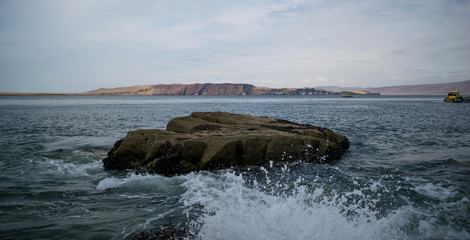 Fototapeta premium a rock in the sea facing an island in the day