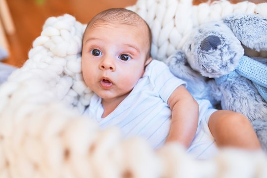 Adorable baby lying down over blanket on the floor at home. Newborn relaxing and resting comfortable with teddy bear