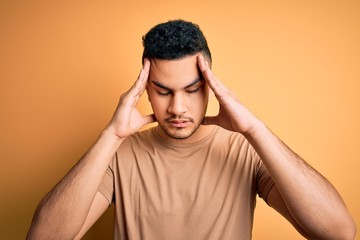 Young handsome man wearing casual t-shirt standing over isolated yellow background with hand on head for pain in head because stress. Suffering migraine.