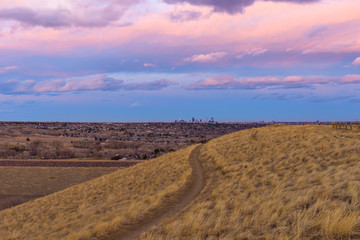 Fototapeta na wymiar Sunset Hiking Trail - Colorful winter sunset view of a hiking trail winding at hillside, with Denver downtown skyline in background. Denver-Lakewood, Colorado, USA.