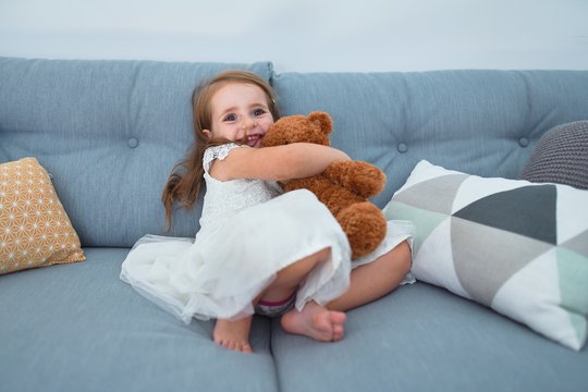 Adorable blonde toddler smiling happy. Sitting on the sofa playing with teddy bear at home