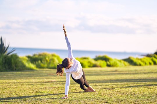 Young beautiful sportwoman practicing yoga. Coach teaching side plank pose at park