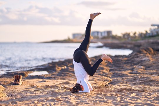 Young beautiful sportwoman practicing yoga. Coach teaching headstand pose at the beach