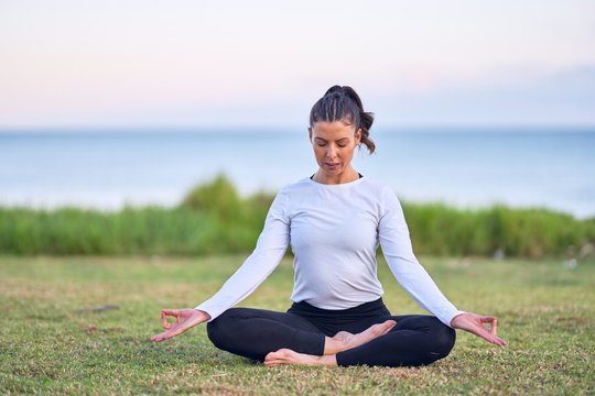 Young beautiful sportwoman practicing yoga. Coach sitting teaching lotus pose at park