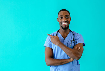Portrait of a smiling male doctor or nurse pointing with finger  to side at studio copy space and looking at camera - obrazy, fototapety, plakaty