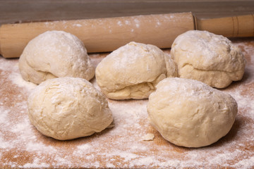 Balls of dough. Plywood cutting board, wooden flour sieve and wooden rolling pin - tools for making dough.