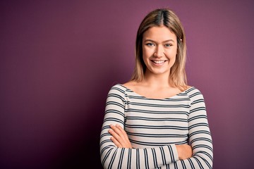 Obraz premium Young beautiful blonde woman wearing casual striped shirt over purple isolated background happy face smiling with crossed arms looking at the camera. Positive person.