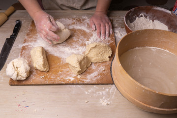 Fototapeta premium A woman kneads the dough. Plywood cutting board, wooden flour sieve and wooden rolling pin - tools for making dough.