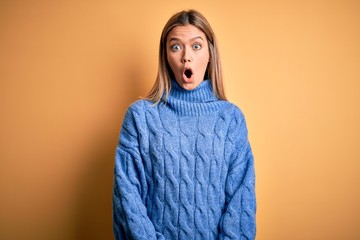 Young beautiful blonde woman wearing turtleneck sweater over yellow isolated background afraid and shocked with surprise expression, fear and excited face.