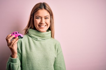 Young beautiful woman holding small toy car standing over isolated pink background with a happy face standing and smiling with a confident smile showing teeth