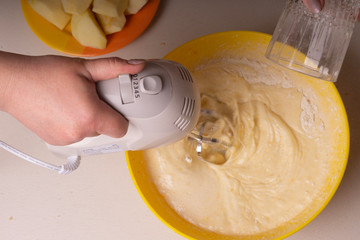 A woman mixes the ingredients for a pie in a yellow bowl with an electric mixer.