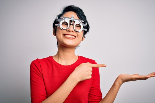 Young beautiful asian girl wearing optometry glasses standing over isolated white background amazed and smiling to the camera while presenting with hand and pointing with finger.