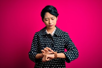 Young beautiful asian girl wearing casual jacket standing over isolated pink background Checking the time on wrist watch, relaxed and confident