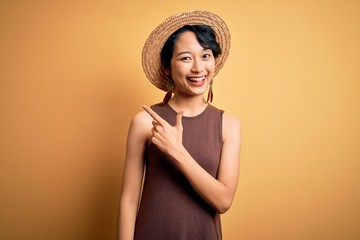 Young beautiful asian girl wearing casual t-shirt and hat over isolated yellow background cheerful...
