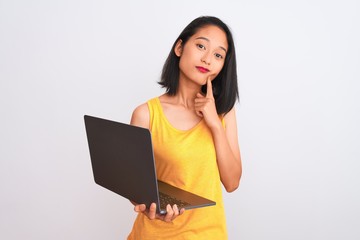 Young beautiful chinese woman using laptop standing over isolated white background serious face...