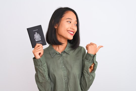 Beautiful chinese woman holding Canada Canadian passport over isolated white background pointing and showing with thumb up to the side with happy face smiling