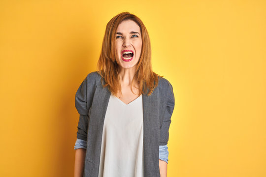 Redhead caucasian business woman over yellow isolated background Shouting angry out loud with hands over mouth