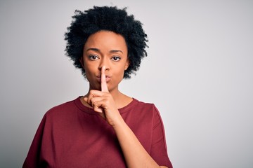 Young beautiful African American afro woman with curly hair wearing casual t-shirt standing asking to be quiet with finger on lips. Silence and secret concept.