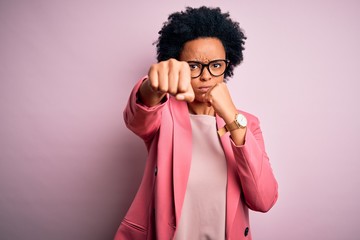 Young beautiful African American afro businesswoman with curly hair wearing pink jacket Punching fist to fight, aggressive and angry attack, threat and violence