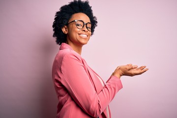 Young beautiful African American afro businesswoman with curly hair wearing pink jacket pointing...
