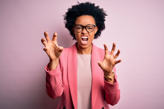 Young beautiful African American afro businesswoman with curly hair wearing pink jacket smiling funny doing claw gesture as cat, aggressive and sexy expression