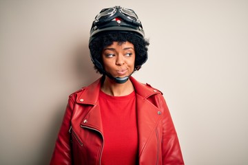 Young African American afro motorcyclist woman with curly hair wearing motorcycle helmet smiling looking to the side and staring away thinking.